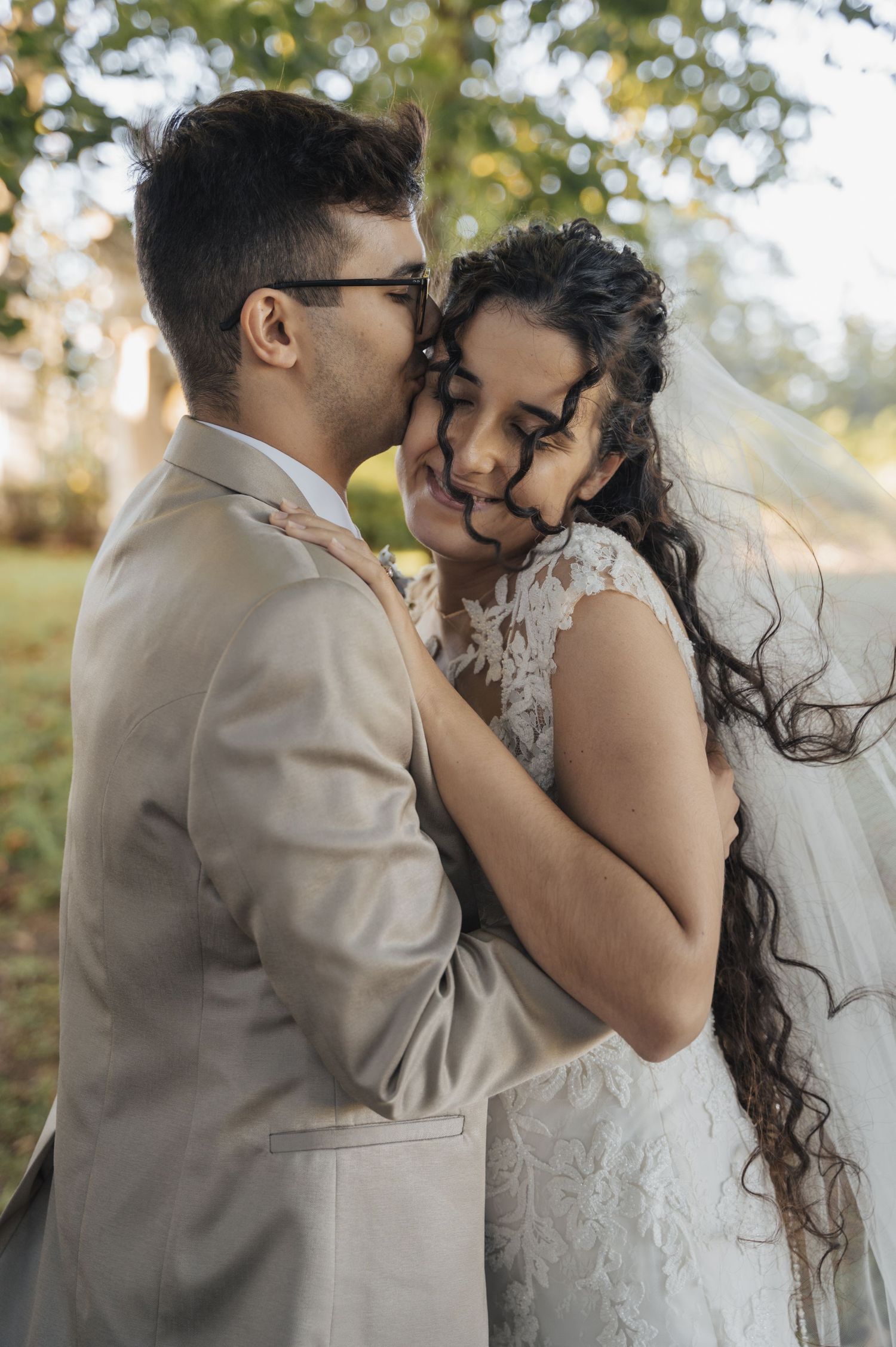 Intimate wedding portrait of couple in formal attire sharing tender moment outdoors.