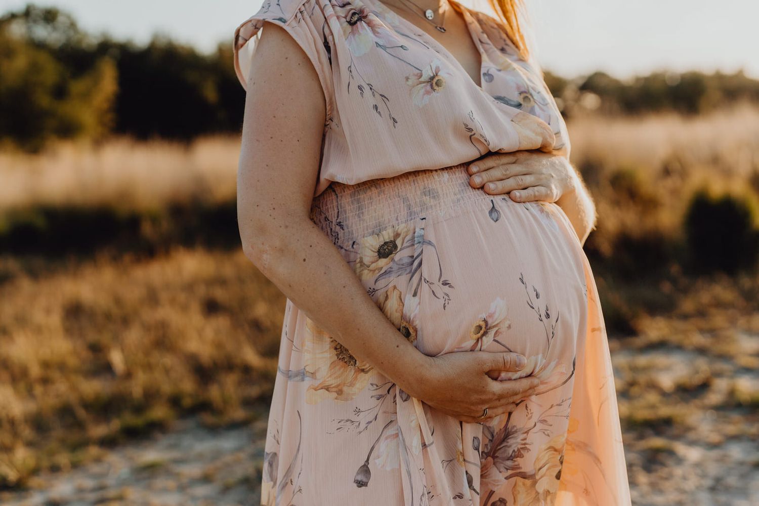 A maternity photo in a floral dress during golden hour in a rural setting.