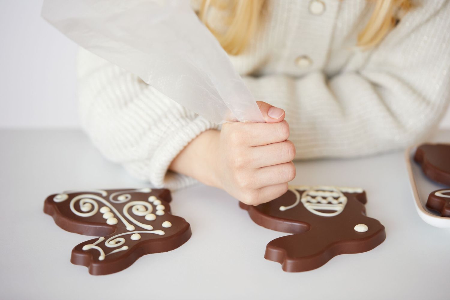 Hands decorating chocolate gingerbread cookies on white surface.