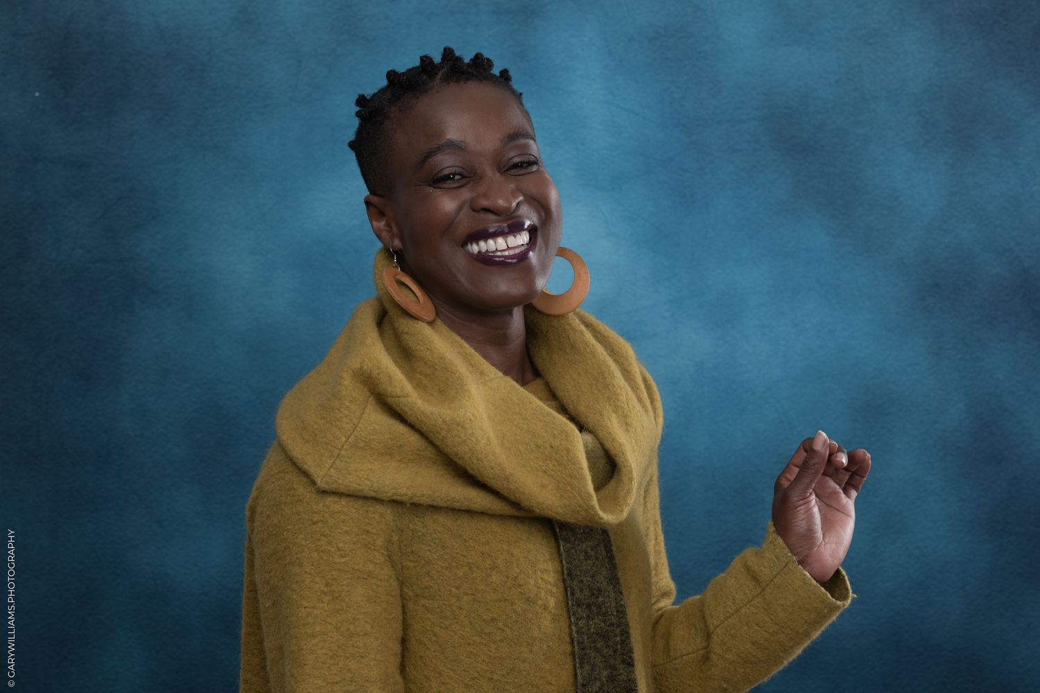 A beautiful black woman smiles for a headshot against a blue background.