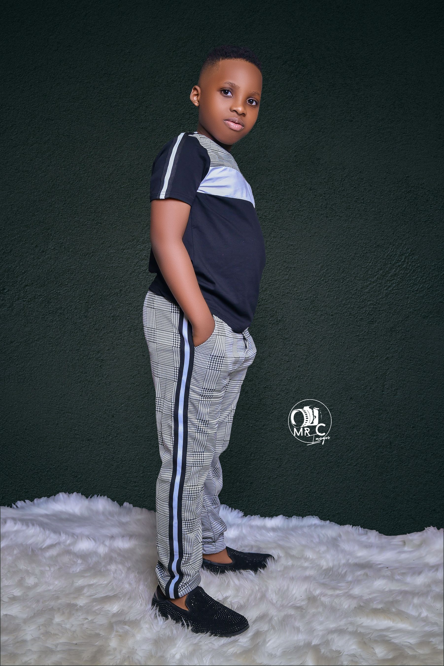 Child in navy and white athletic wear with grey striped pants posing against dark background.