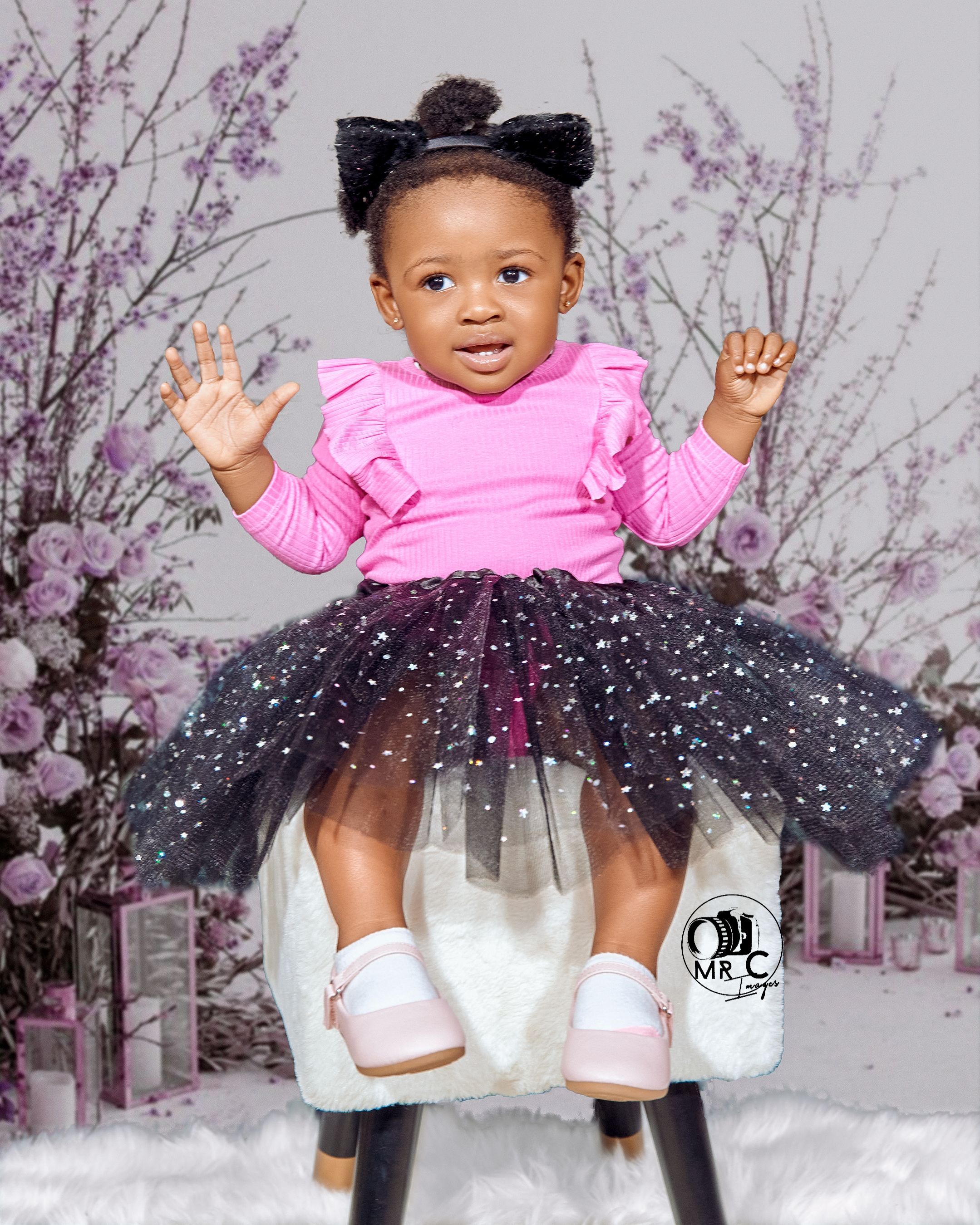 Baby in pink top and sparkly black tutu posing with cherry blossoms in background.