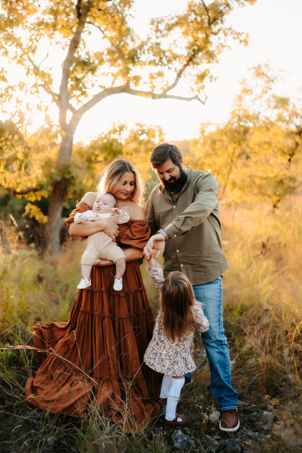 Family of four poses together in autumn field with golden foliage.