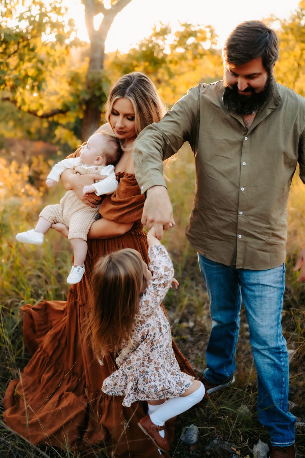 A tender family moment captured outdoors during sunset with golden autumn trees in the background.