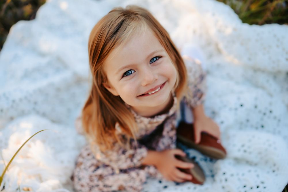 Closeup of happy girl in floral dress lying on white lace blanket outdoors.