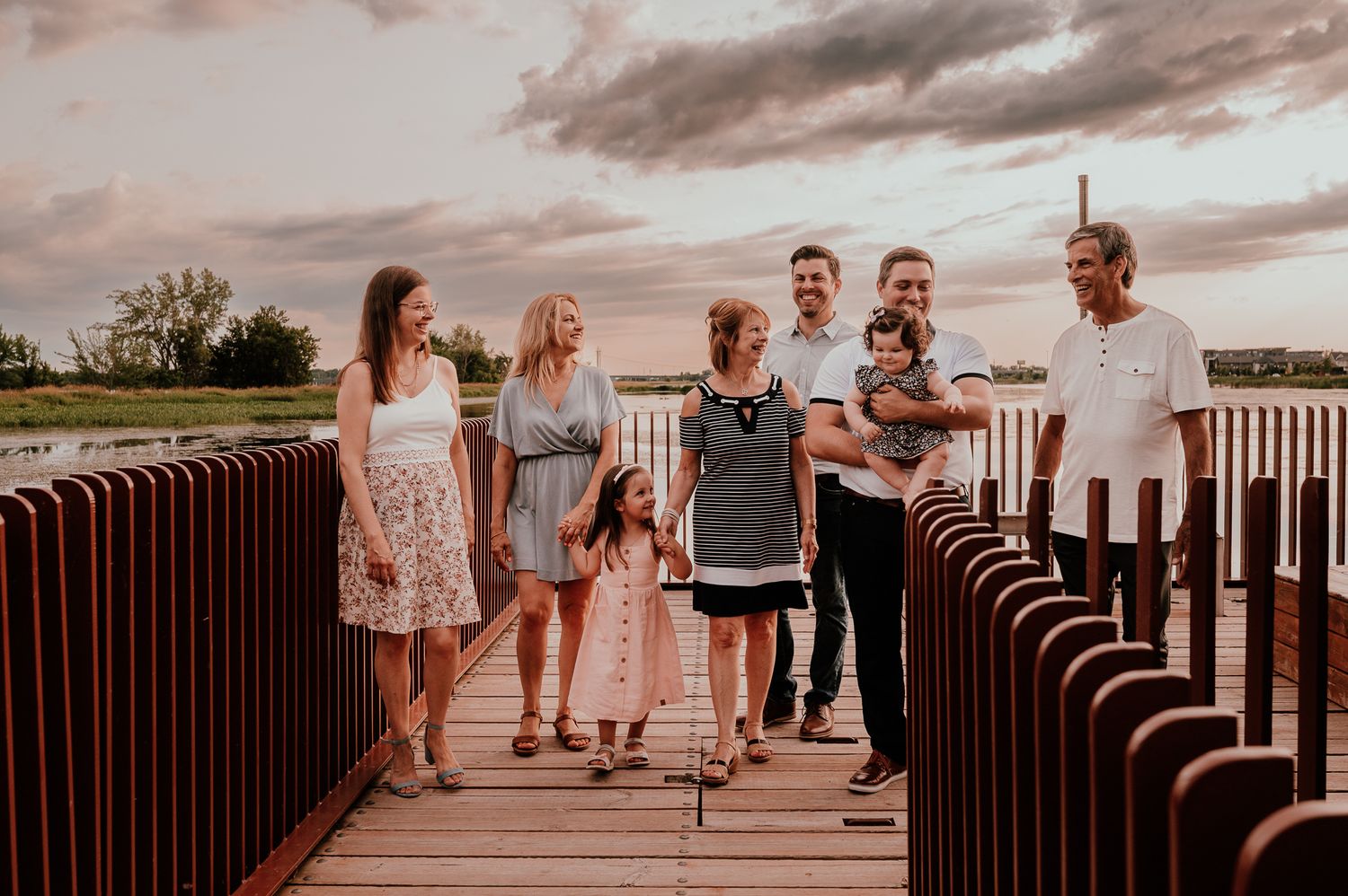 A group of people standing on a wooden boardwalk at sunset.