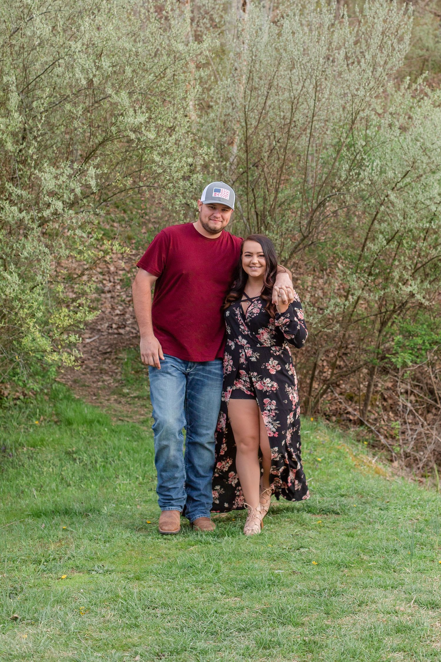 Couple walking together on grass path wearing casual clothing and floral dress.