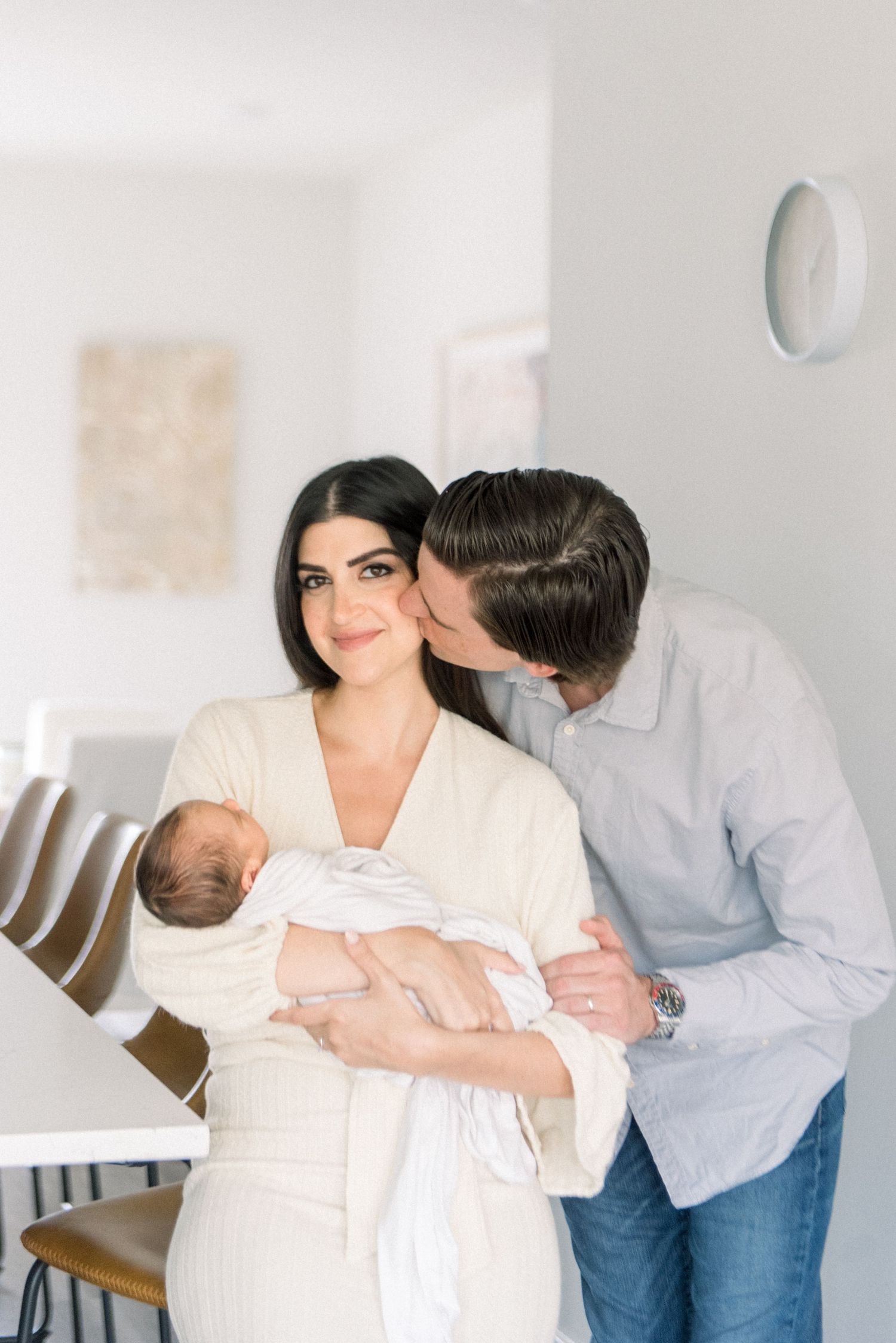 An intimate family portrait in a bright dining room with a sleeping newborn.