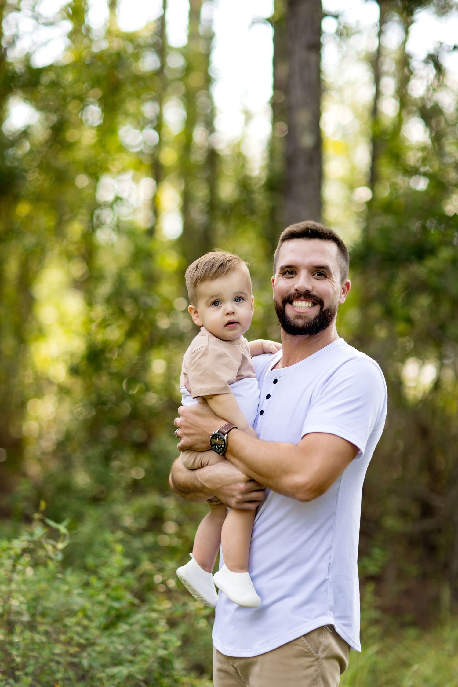 Outdoor photoshoot with father holding toddler against green forest backdrop.