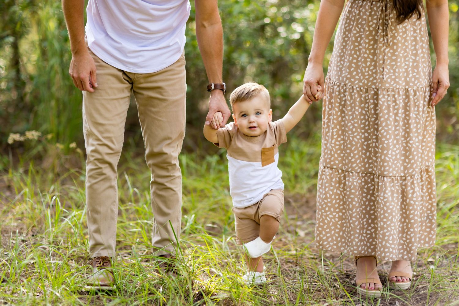 Casual family photo showing legs and feet of parents and child walking through woodland setting.
