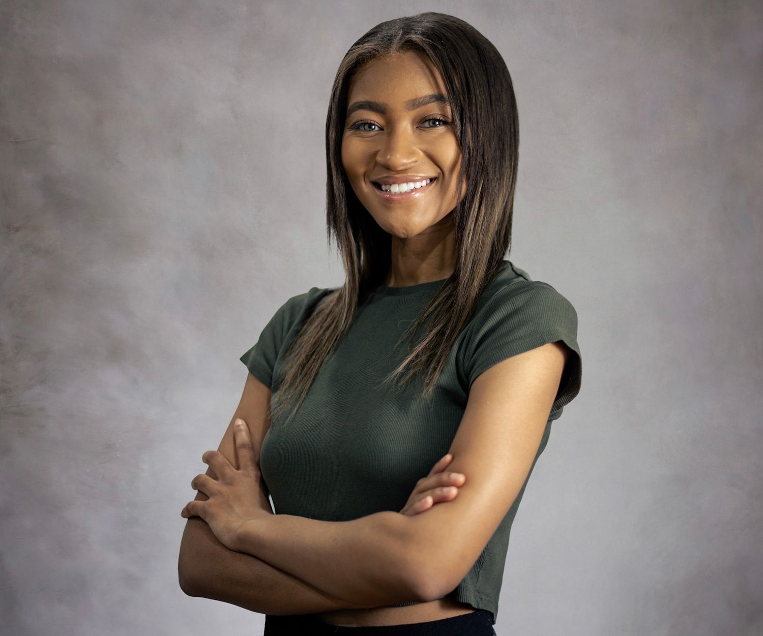 Professional portrait of a smiling woman in a dark green top against a gray backdrop.