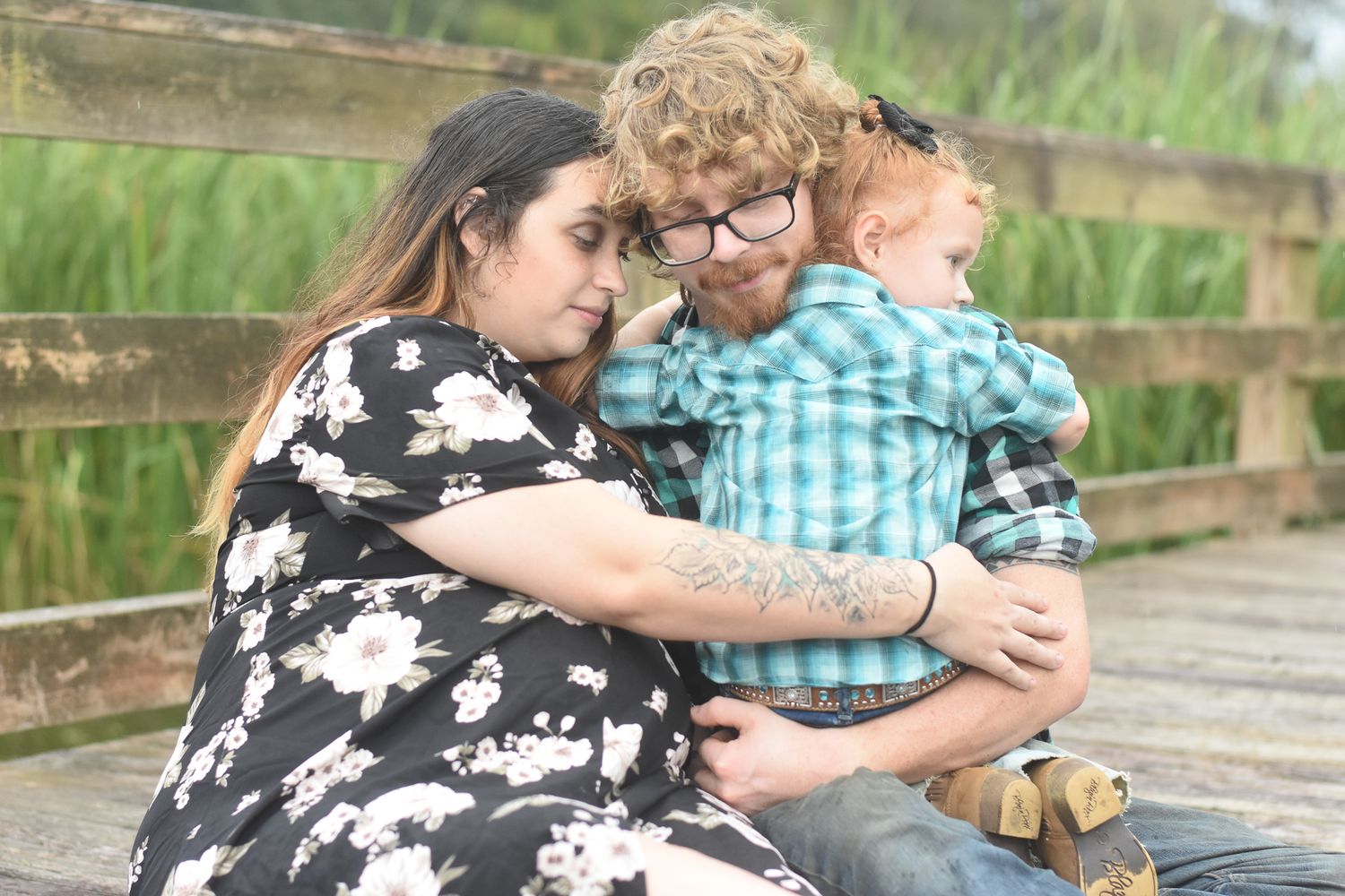 Family sitting together on wooden deck with tall grass in background for outdoor portrait session.