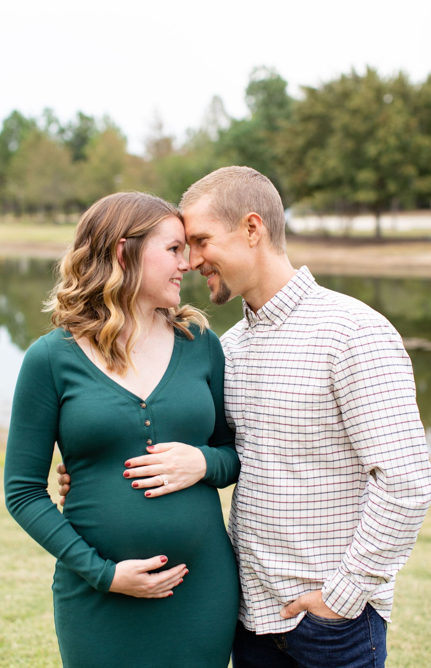 Tender maternity moment captured by a lake with couple in complementary casual outfits.