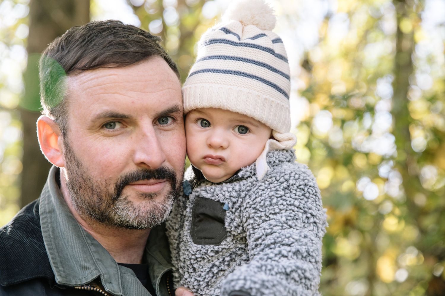 Outdoor portrait of baby in warm winter clothing with adult against natural background.