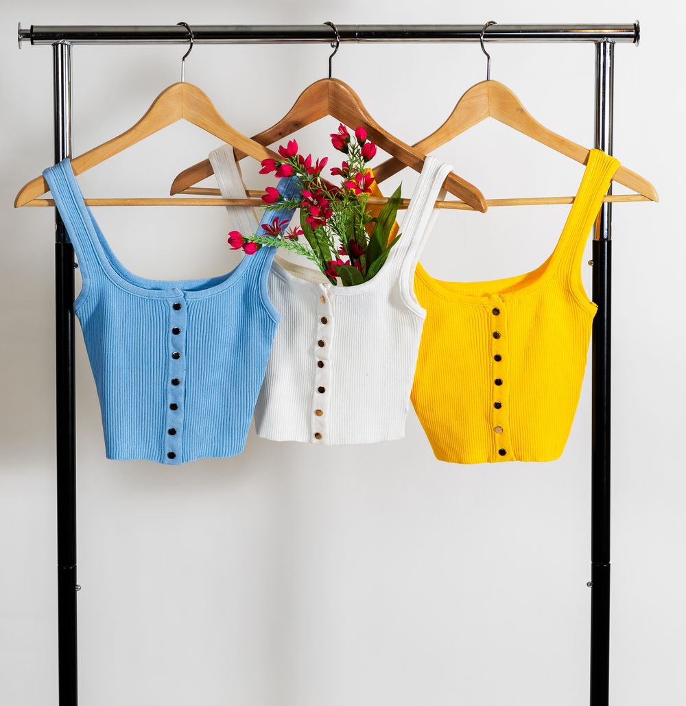 Product shots of 3 tank tops that are blue, white and yellow along with some pink flowers all on hangers