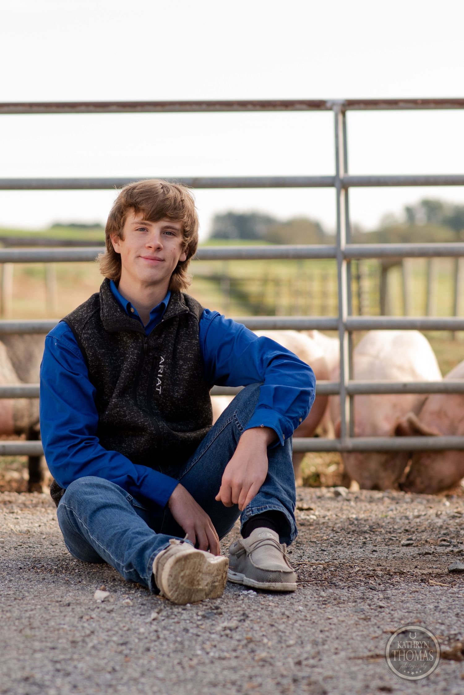 A casual portrait shows someone in a blue jacket and fleece vest sitting near farm equipment.