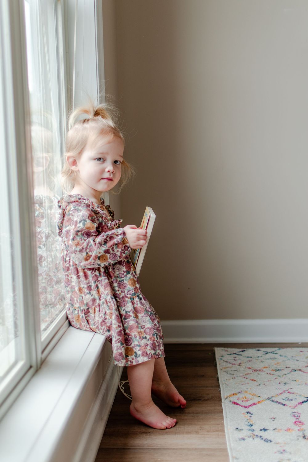 A sweet girl sits on the window sill reading her favorite book.