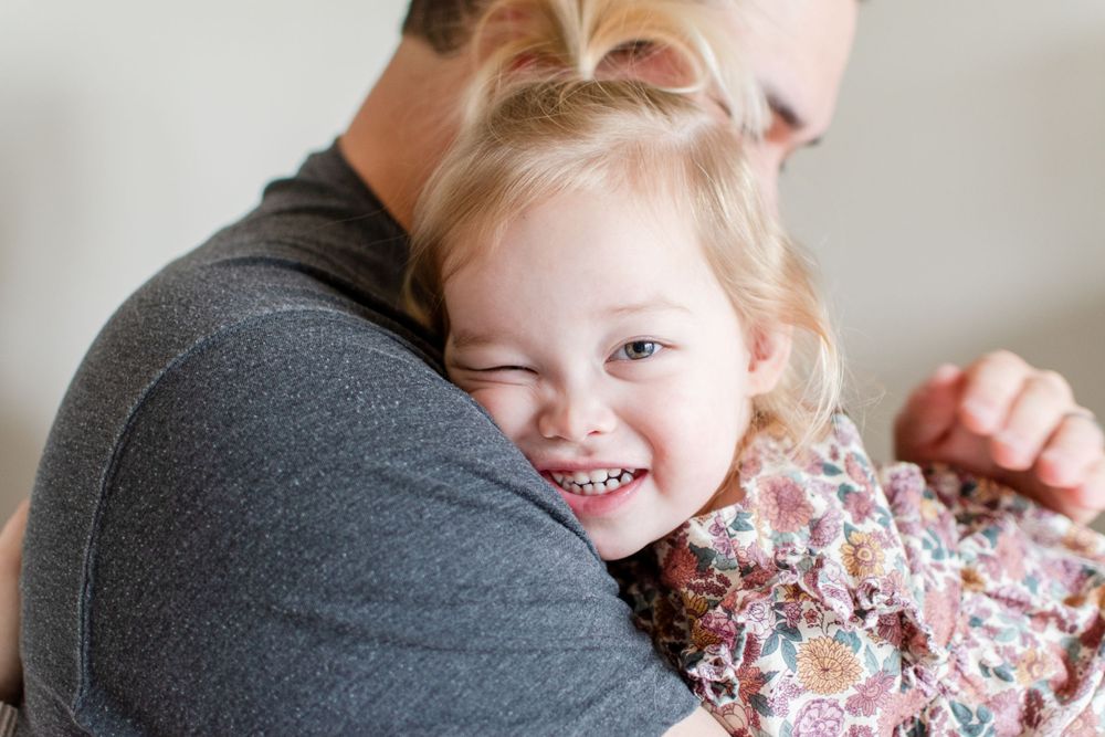 A sweet little girl snuggles close to her daddy, squishing her cheek against his shoulder.