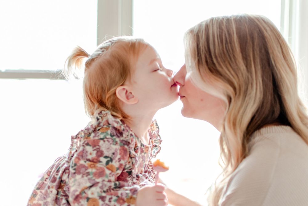 A little girl gives her mom a kiss on the nose.