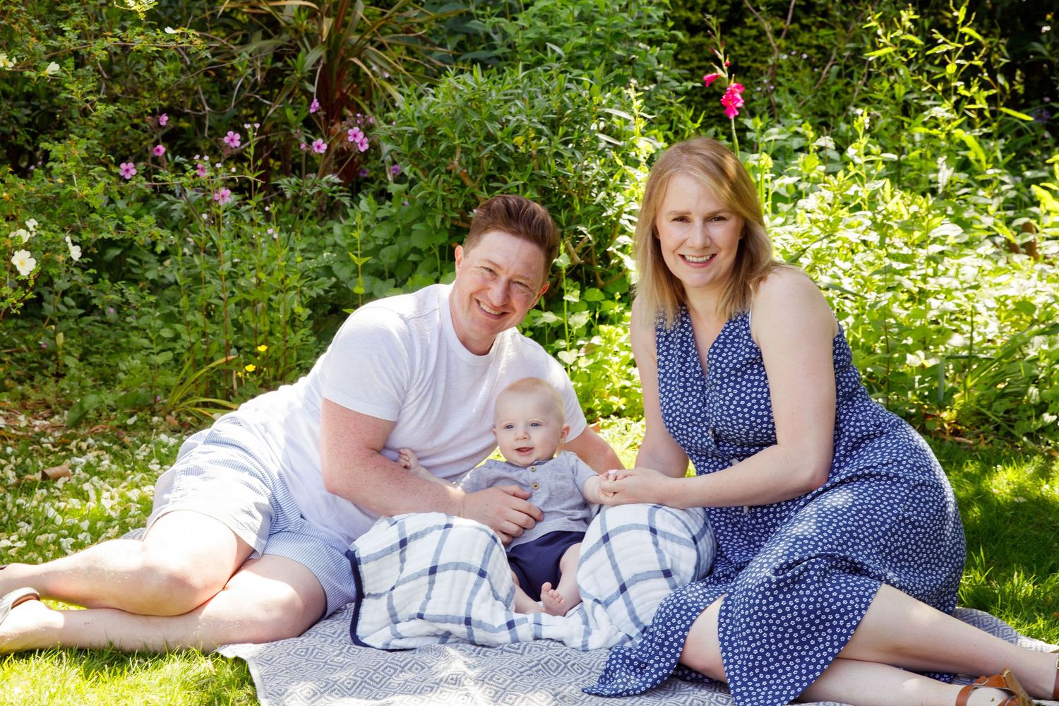 Family picnic on a blanket in a sunny garden with party decorations.