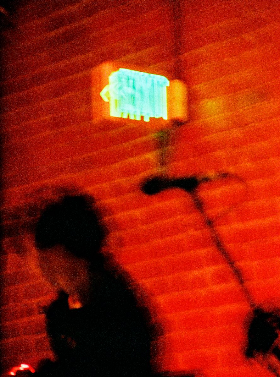 Silhouetted figure against brick wall with glowing blue exit sign overhead.
