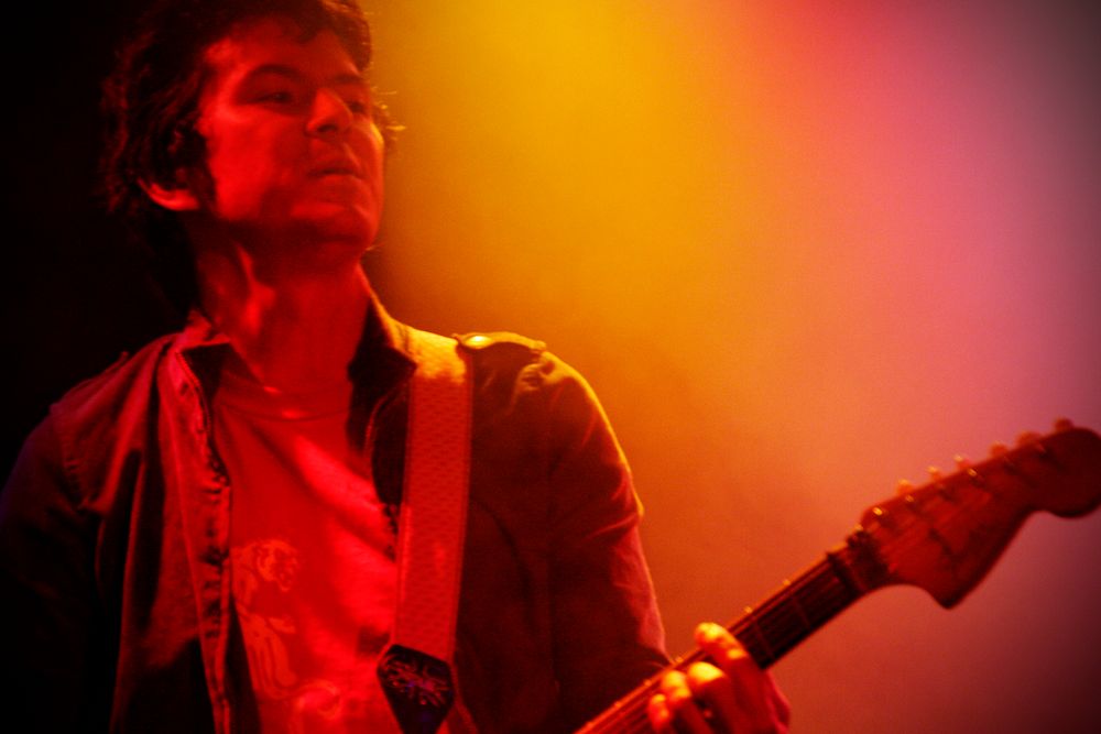 A guitarist performs on stage bathed in dramatic red and orange lighting.