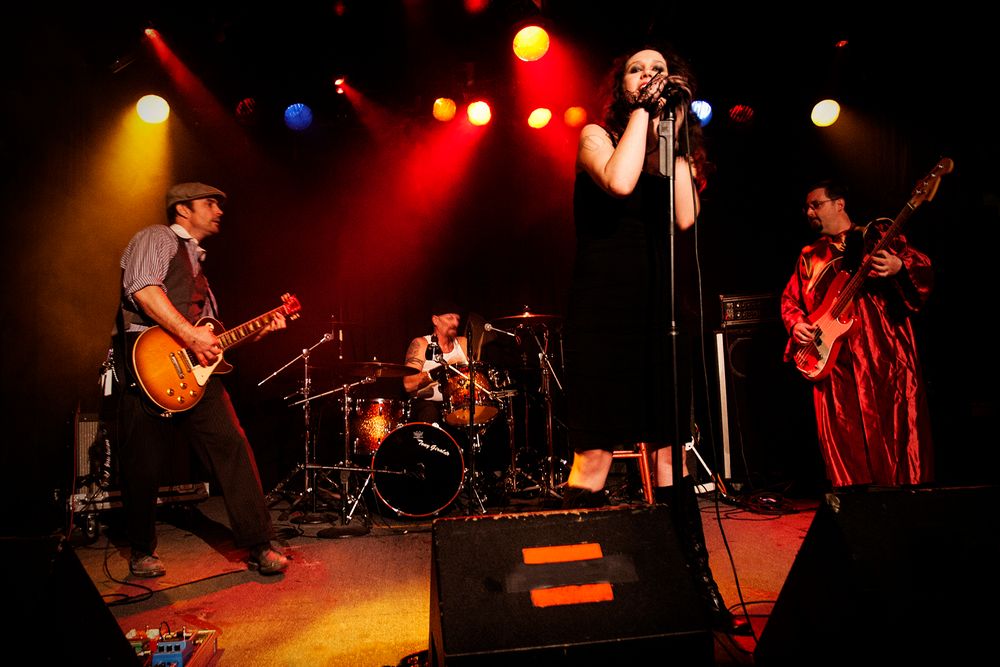 A full band performs on stage with colorful spotlights creating a dynamic concert atmosphere.