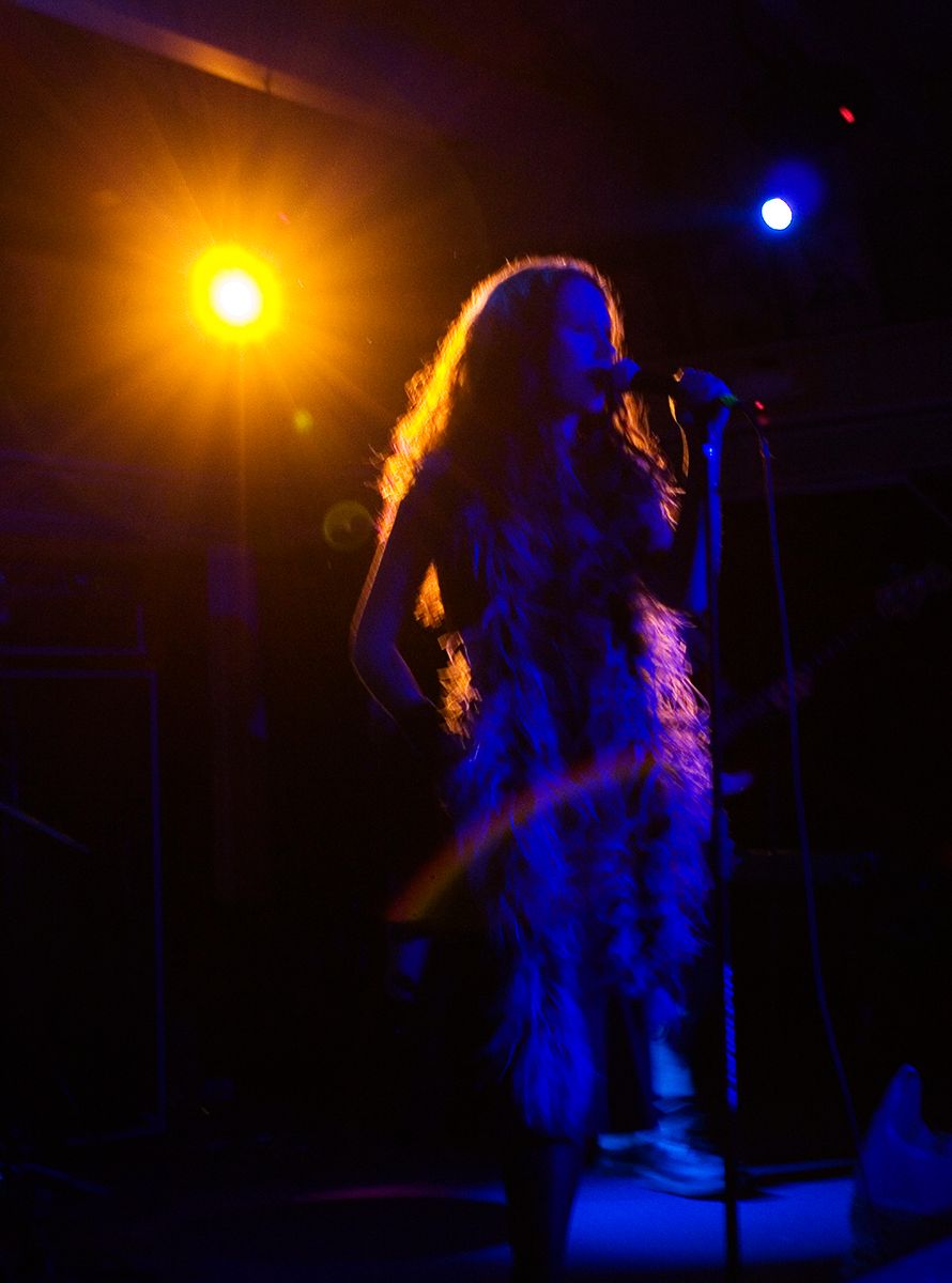 A silhouetted performer sings on stage illuminated by dramatic orange and blue lighting.