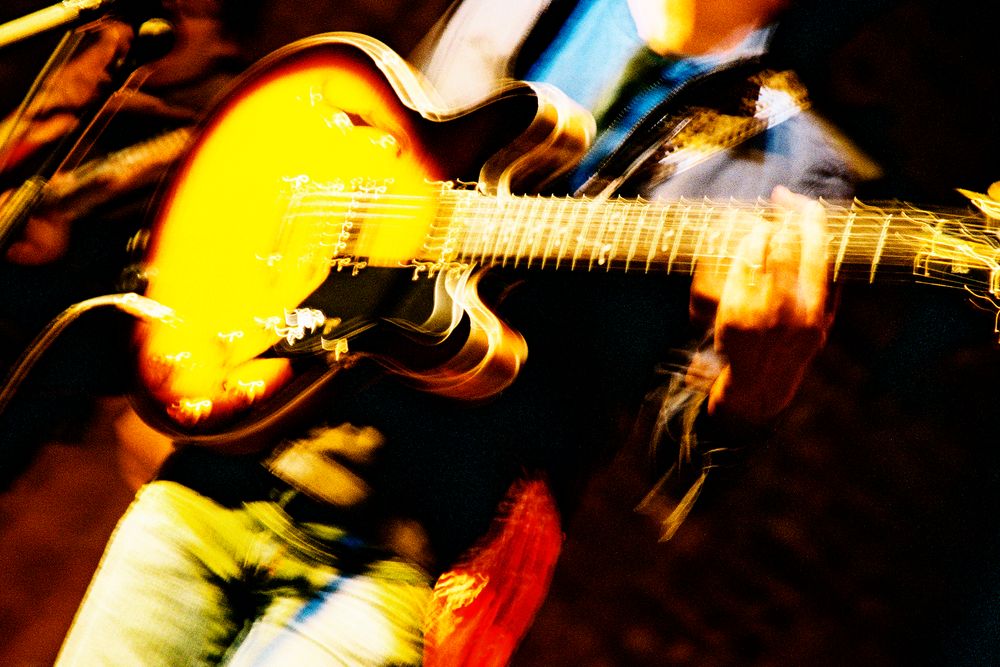 Close-up of hands playing a sunburst guitar with motion blur creating a dynamic effect.