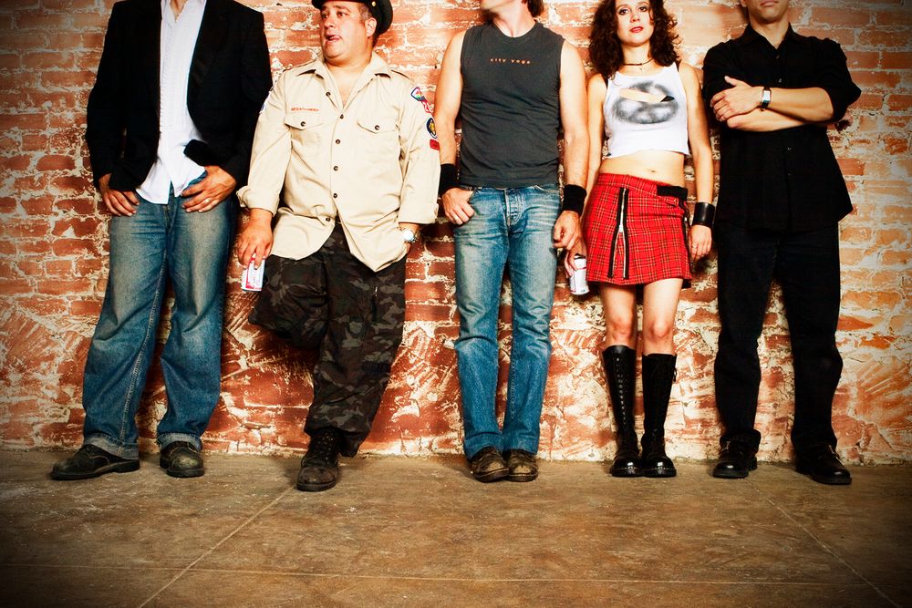 Group standing against brick wall showing only lower bodies in casual clothing.