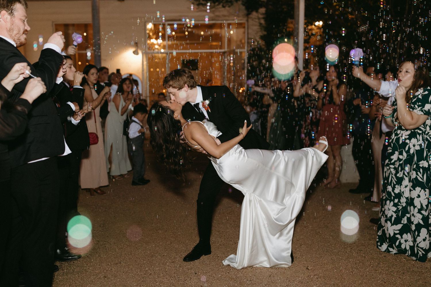 A romantic dance dip during a wedding reception with festive lights and guests in the background.