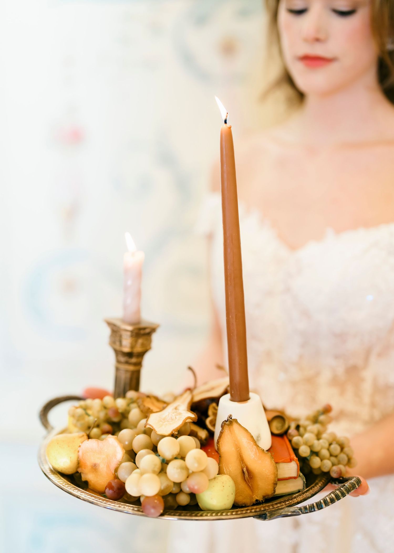 Elegant still life with lit taper candles and fresh fruit on antique brass tray.