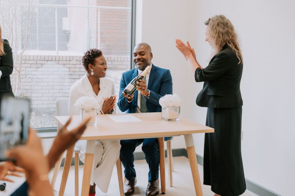 Guests celebrate and applaud during an intimate ceremony in a bright room.