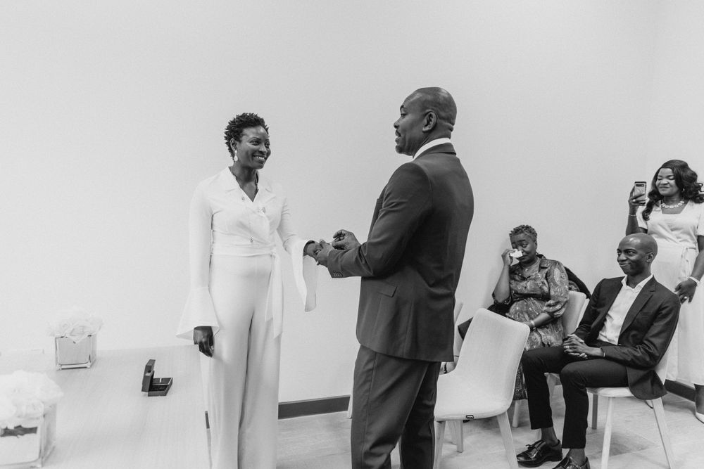 A couple participates in a ceremony while others watch seated in the background.