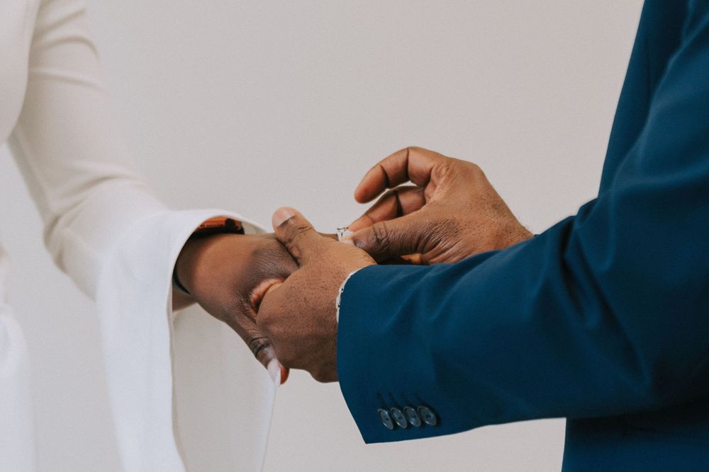 Hands exchange rings in an intimate ceremony against a white background.
