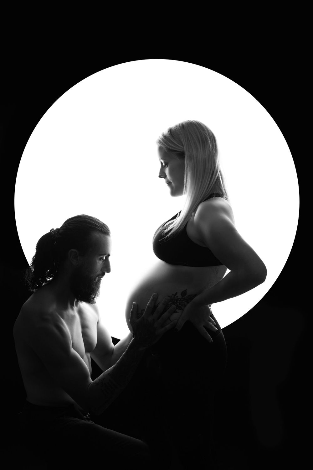 Artistic black and white maternity silhouettes against oval window backdrop.