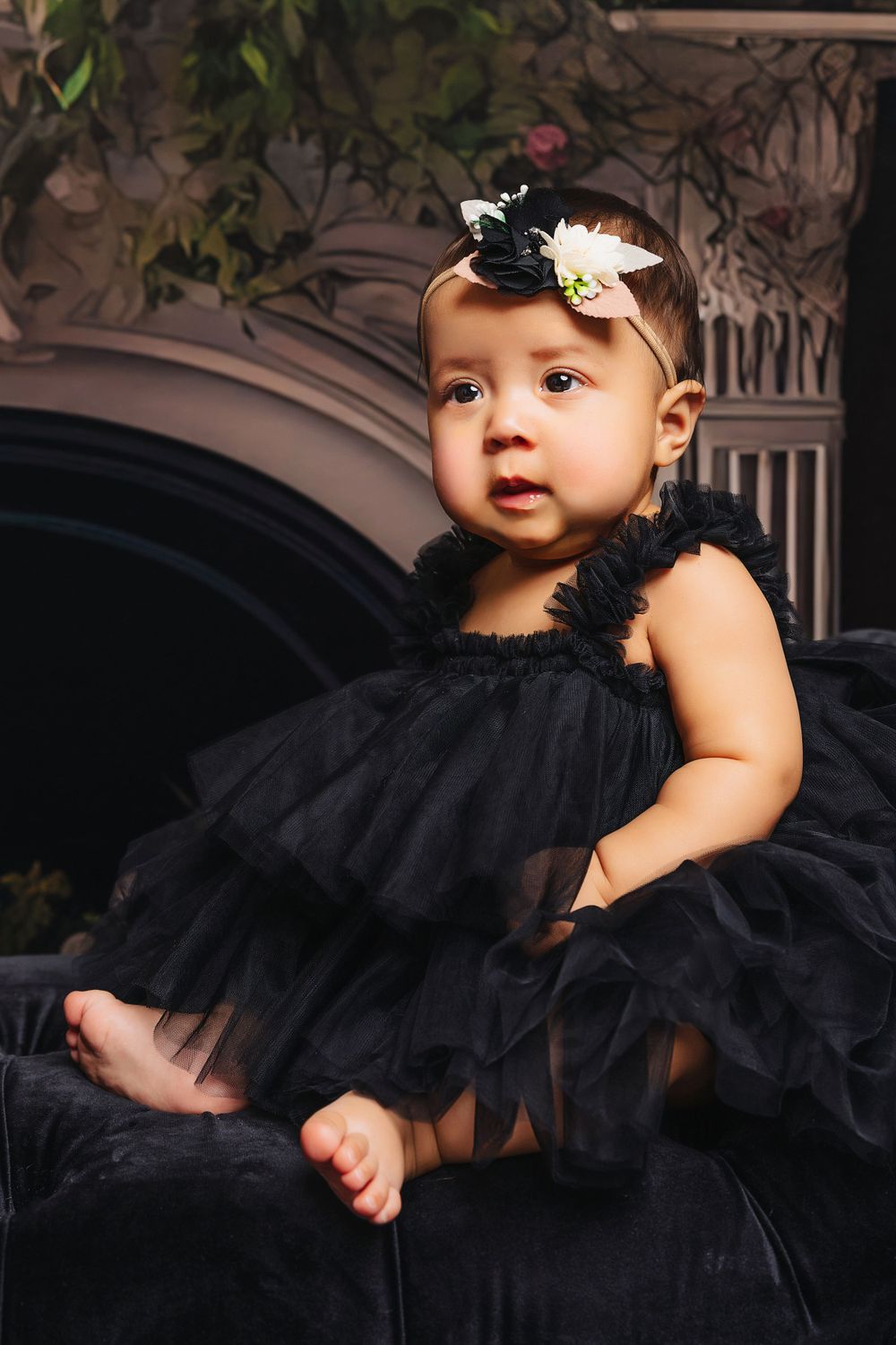 Small child wearing black tulle dress and bow headpiece seated on dark couch.
