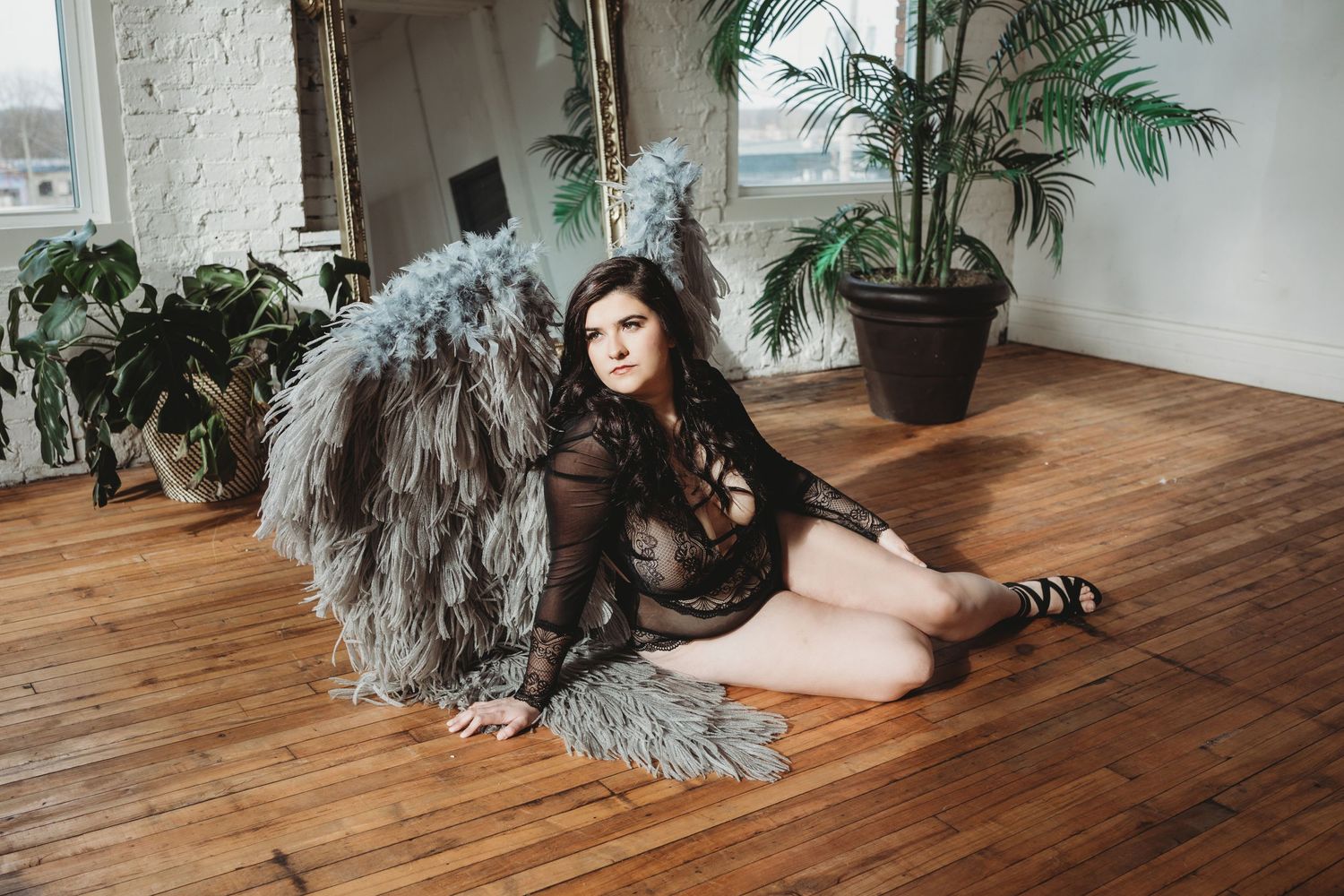 Indoor boudoir photography setup with hardwood floors, white walls, and potted plants.