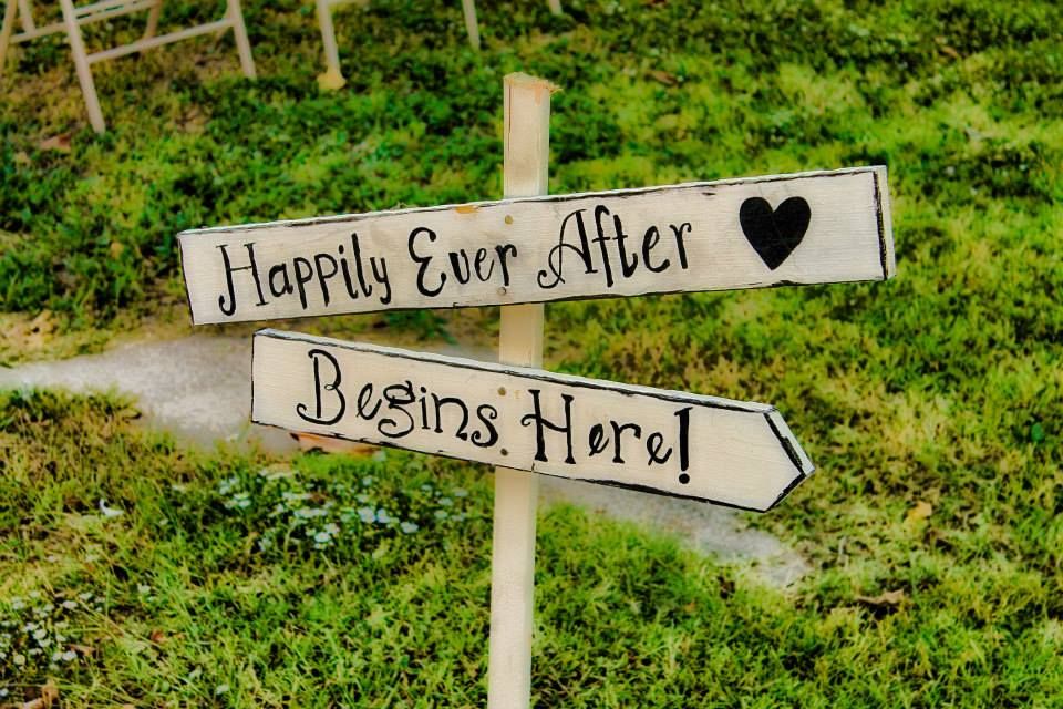 Rustic wooden directional sign reading 'Happily Ever After Begins Here' with heart decoration.