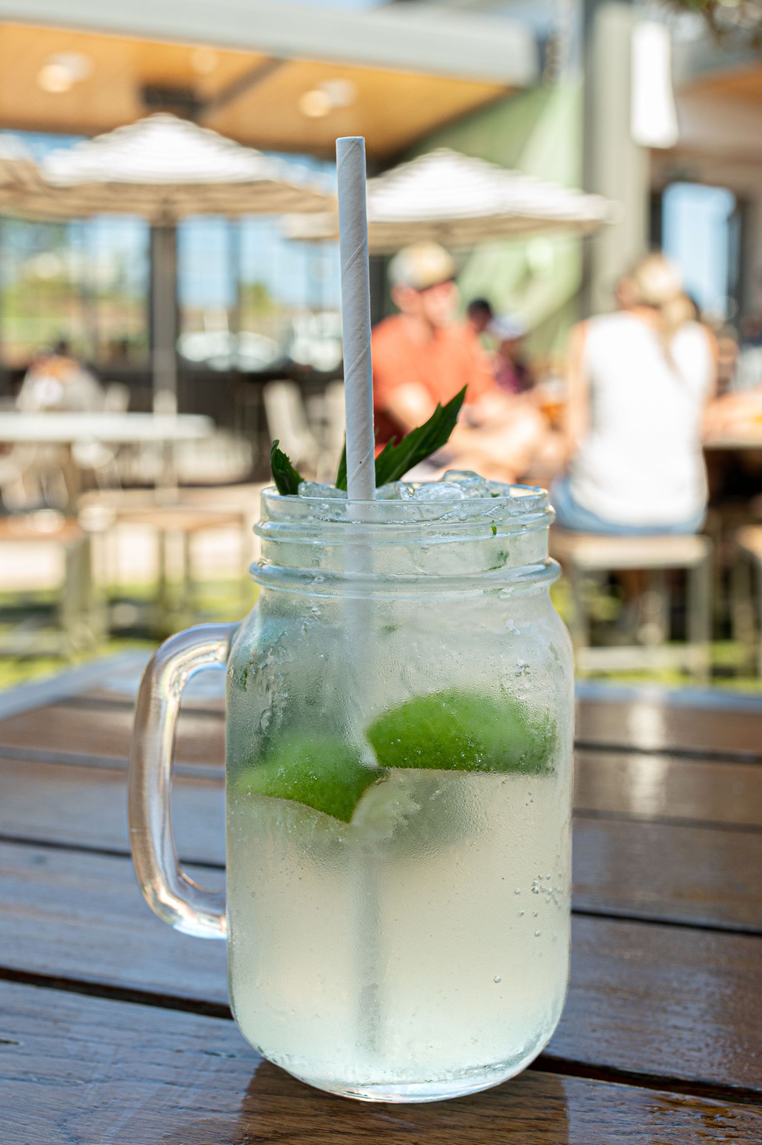 Refreshing limeade served in a mason jar mug on a wooden table outdoors.