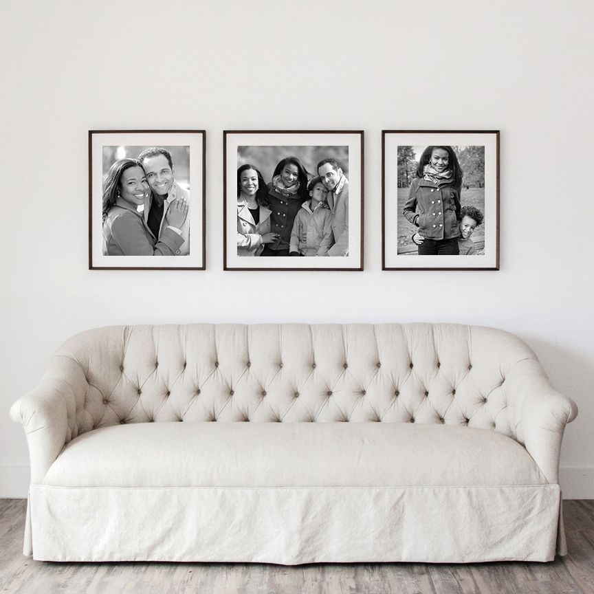 Three black and white family portraits in dark frames displayed above a tufted cream couch.