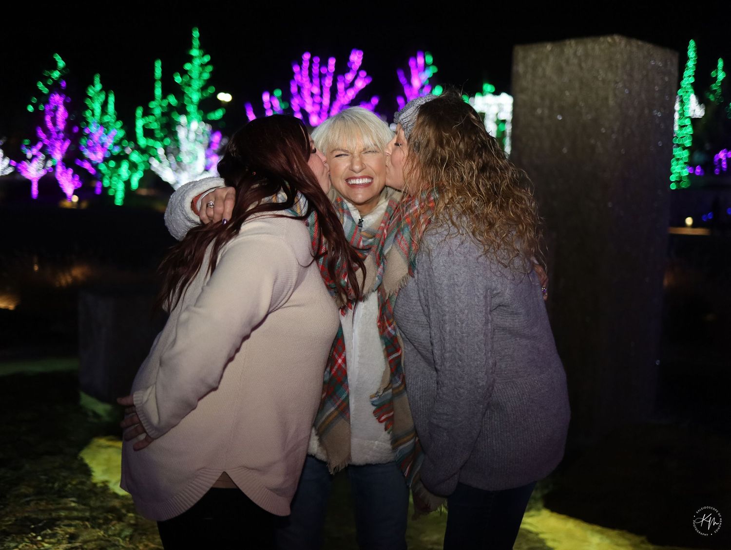 Group photo at nighttime holiday light display with colorful illuminated decorations in background.
