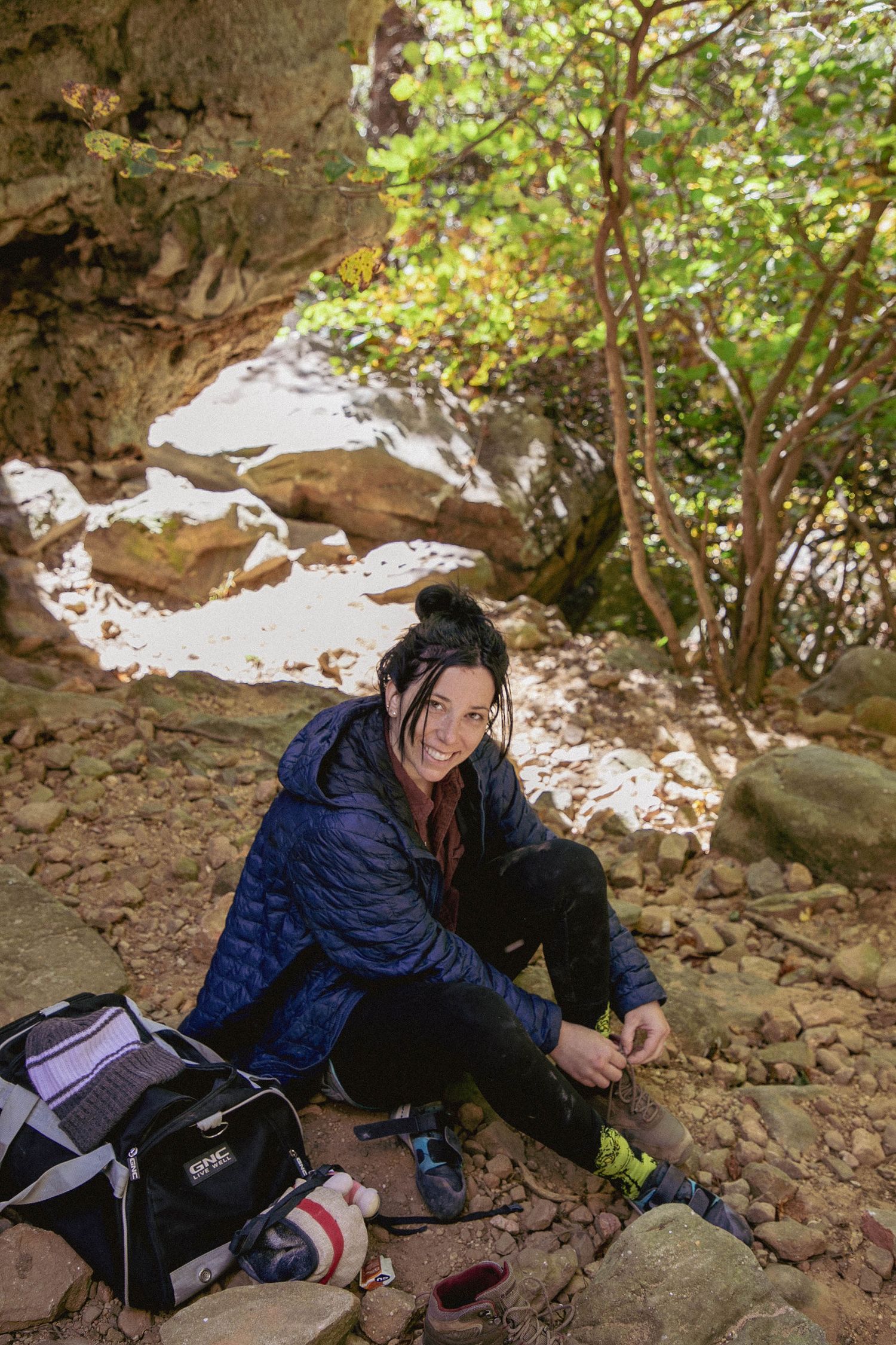 A photographer rests in a cave-like setting with hiking gear and camera equipment.