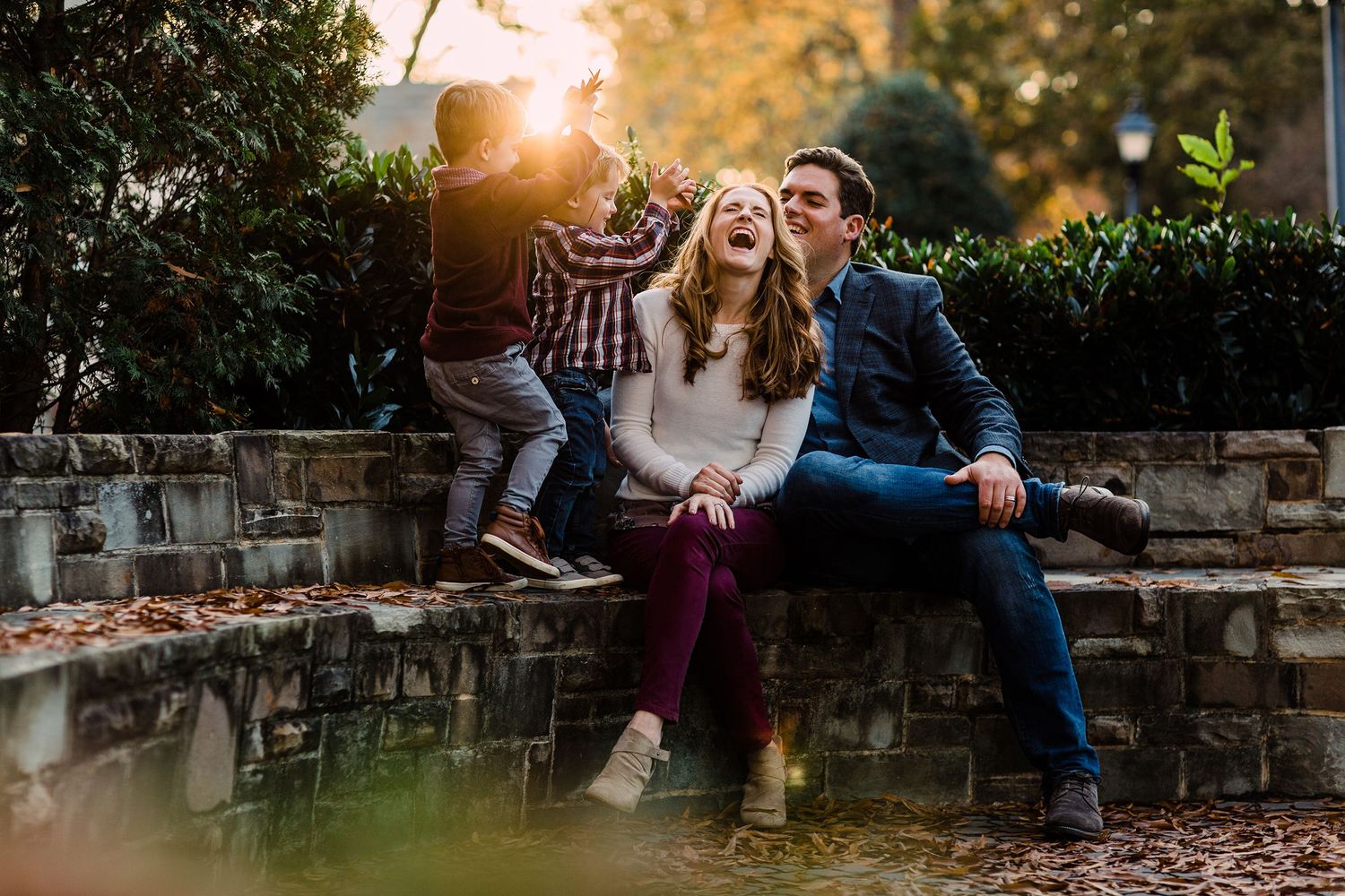 Family sharing joyful moment together on stone wall during autumn sunset.