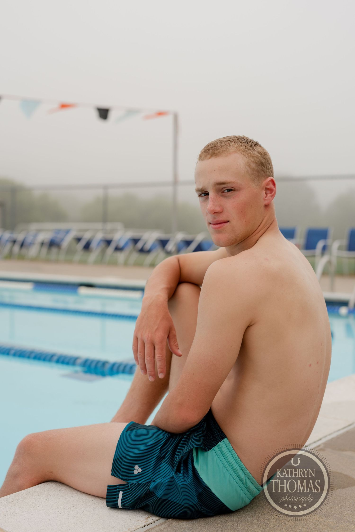 A swimmer rests on the pool deck during an overcast day with pennant flags visible overhead.