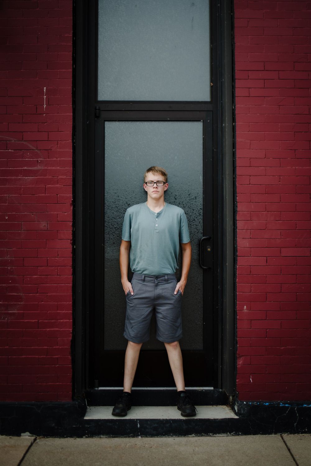 Portrait against red brick wall with grey doorway frame.