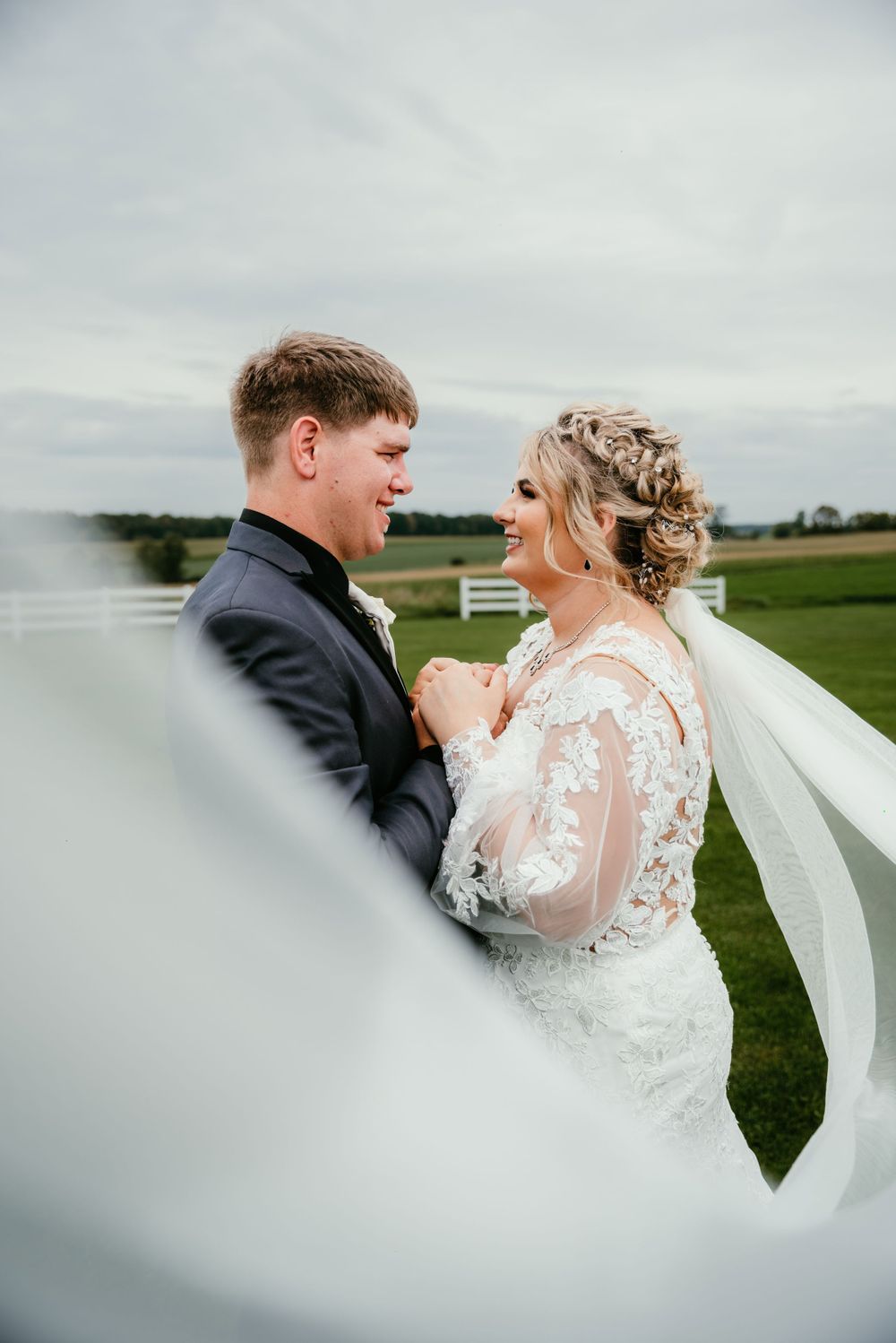 Romantic wedding portrait with flowing veil against countryside backdrop.