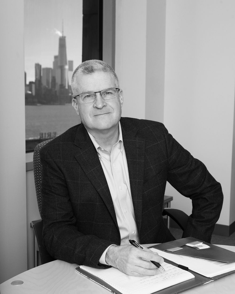 Professional portrait in office with city skyline visible through window.