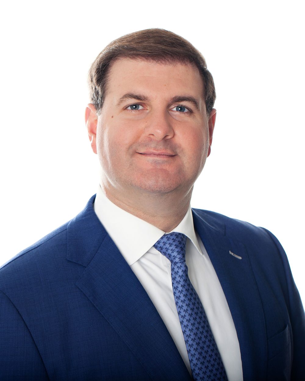 Business portrait of person in navy suit with blue dotted tie against white background.