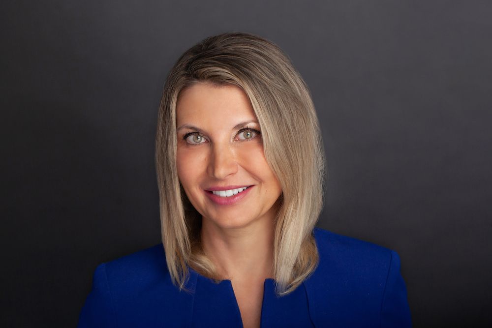Professional headshot portrait in blue blazer against dark background.